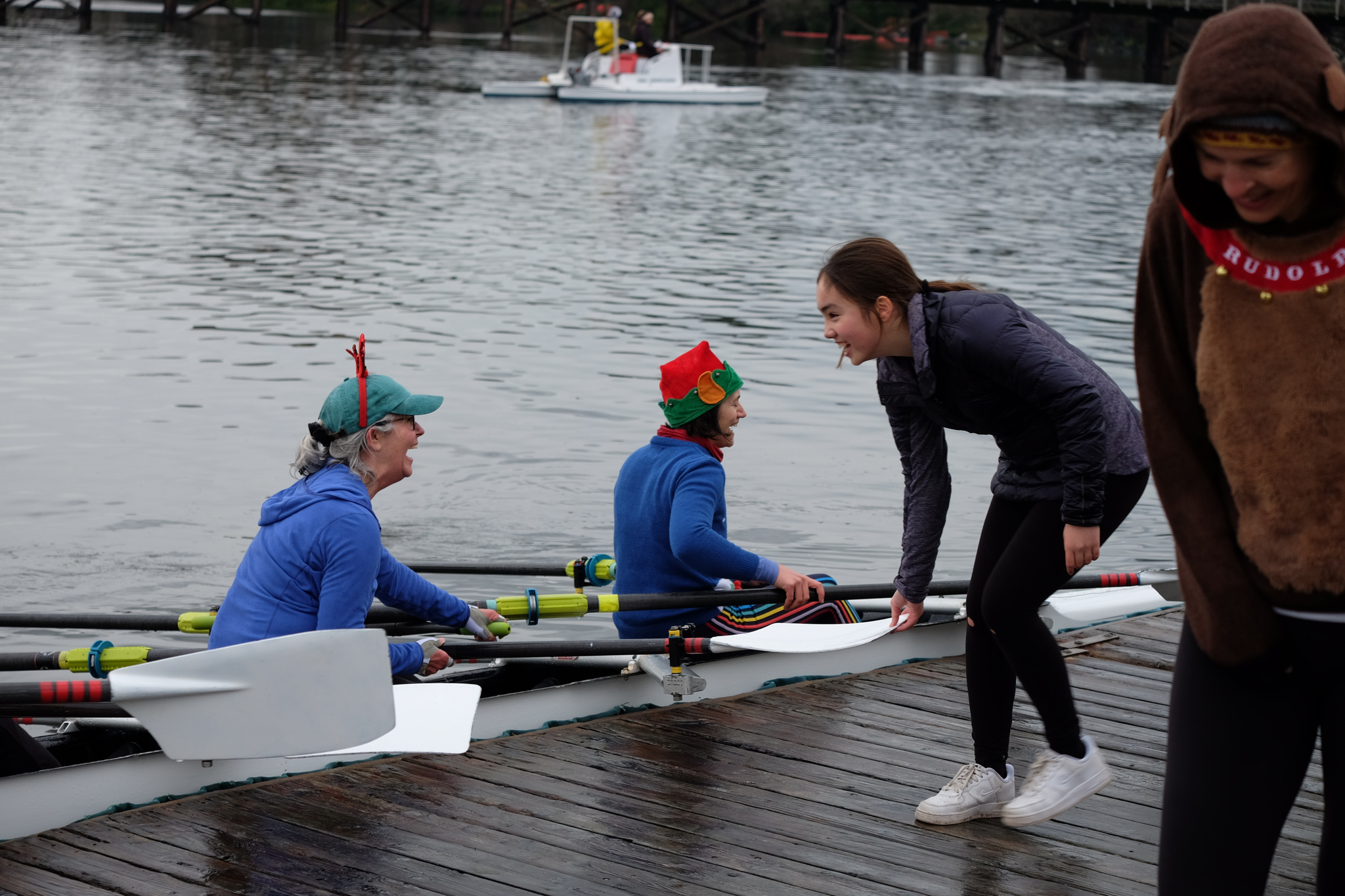 A quad docking. Two rowers are visible, while a third helps bring them in by holding the oar.