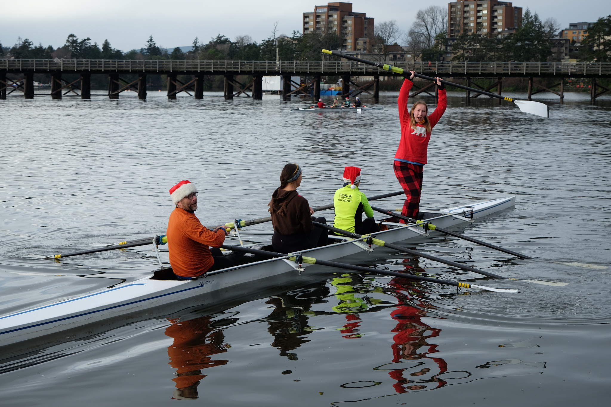 A quad has finished the race. One of the rowers is standing and twirling their oar.