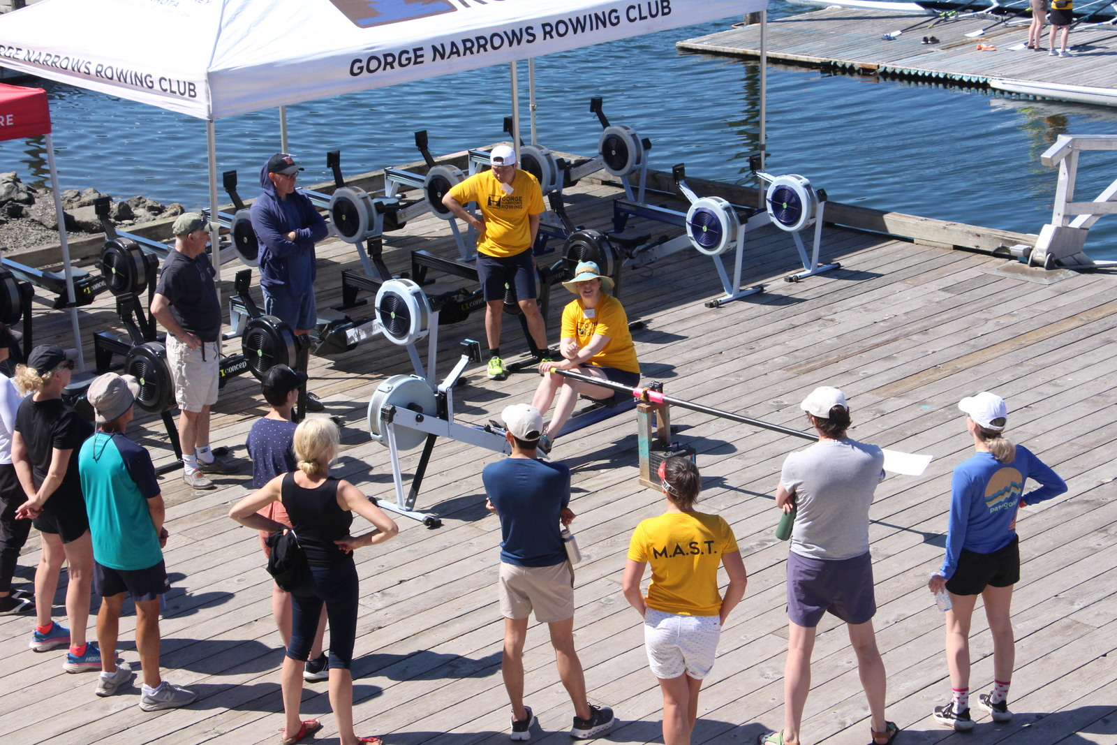 A group getting their first orientation, with rowing machines visible in the background.