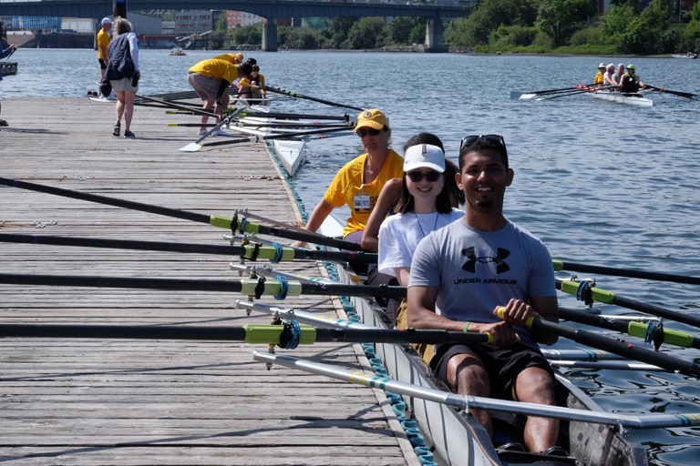 A quad getting ready to push off the dock. Behind is an empty quad and another quad getting ready. A fourth quad is on the water. Several volunteers are on the dock.