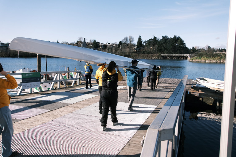 Participants, staff, and volunteers carry a boat down to the water.