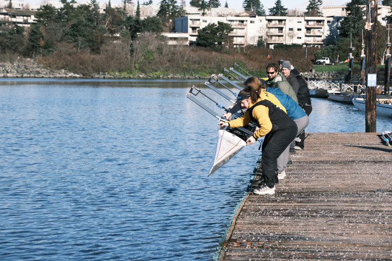 Participants, volunteers, and staff lower a boat into the water.