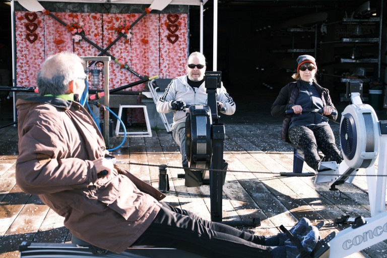 A volunteer instructs two participants in the basics of the stroke on a rowing machine.