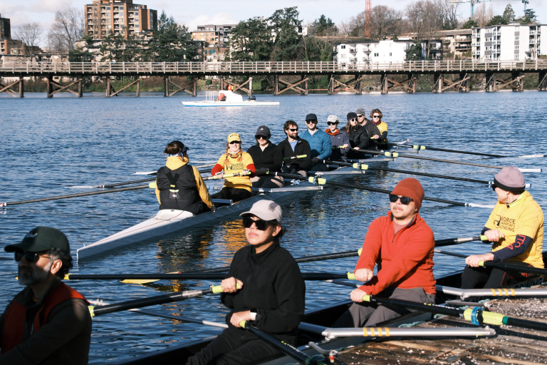 The eight on the water with a quad, preparing to launch, on the dock. In the background is a coach boat and the Selkirk Trestle.