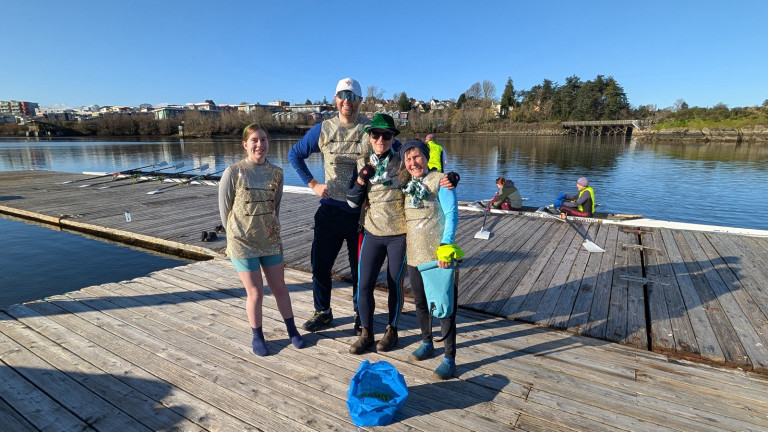 Four racers on the dock. Behind them on the dock are an empty quad, and a second boat with two people visible.